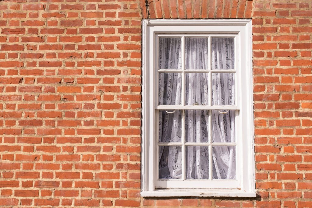 Victorian wooden frame white sash window with glass panels on a classic red brick wall